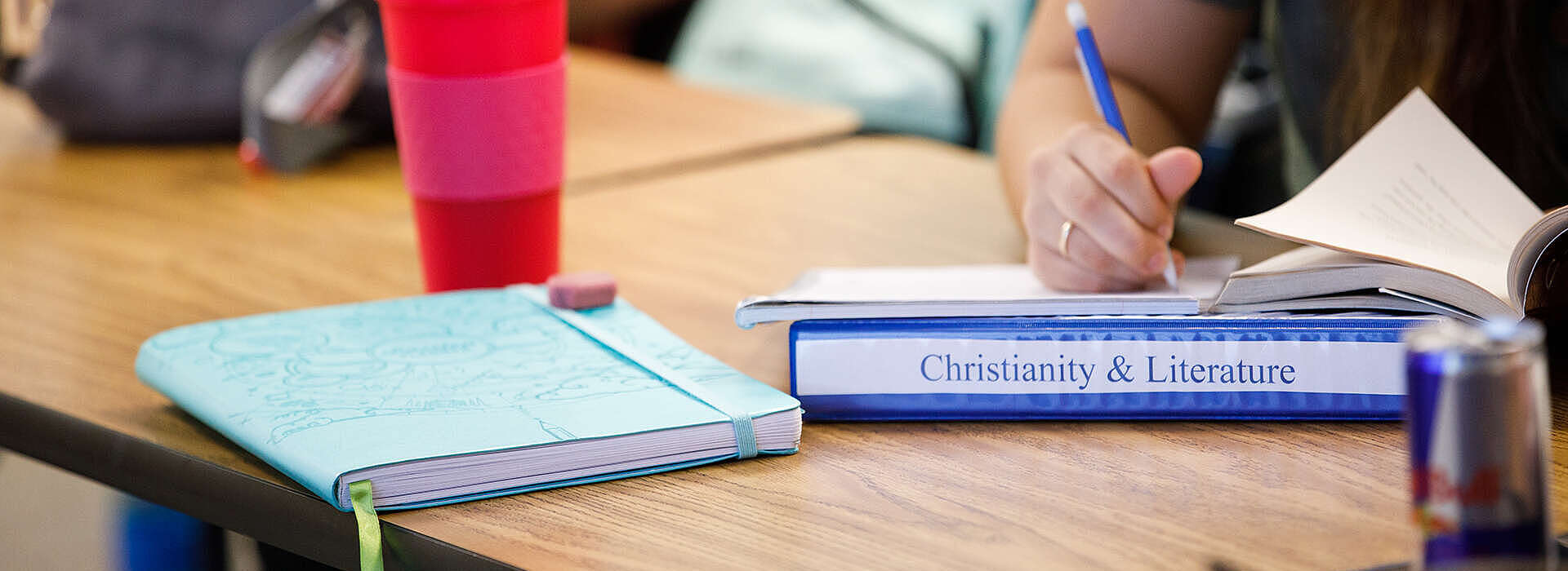 desk with cup and notebooks, one labeled Christianity and Literature
