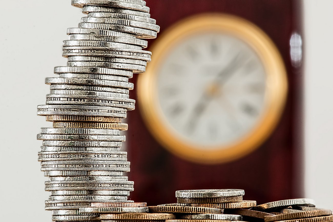 Several coins stacked up with an out of focused clock behind them