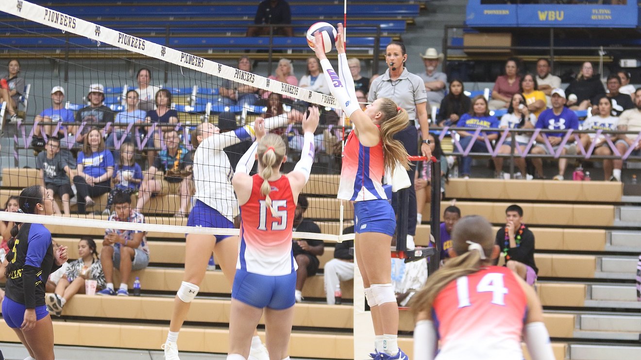 photograph of an LCU volleyball player, Hope Gonsioroski, rising up to block a shot from the opposing team