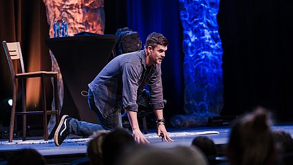 Photograph of Dr. John Delony kneeling on stage with dramatic stage lighting