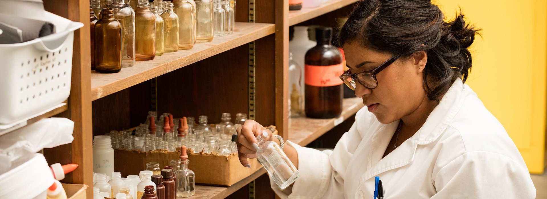 Student in a white lab coat analyzing a glass bottle