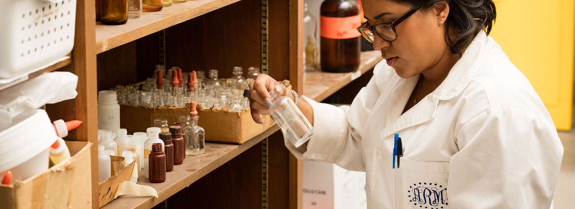 Student in a white lab coat analyzing a glass bottle