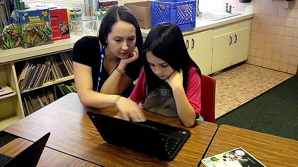 student teacher working with young student on laptop