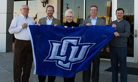 5 staff members on aim bank holding a LCU Flag outside