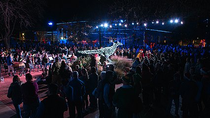 Crowd gathering around the chap on campus under Christmas lights 