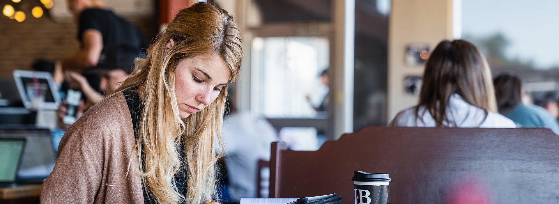 Girl reading through a book taking notes at table in a coffee shop