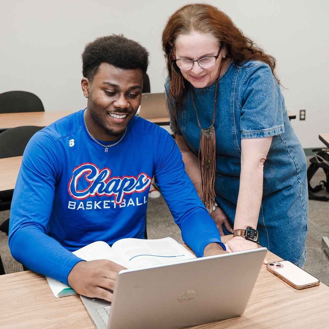 Photograph of Devin Baccas sitting at a desk with Dr. Carroll looking over his shoulder helping him