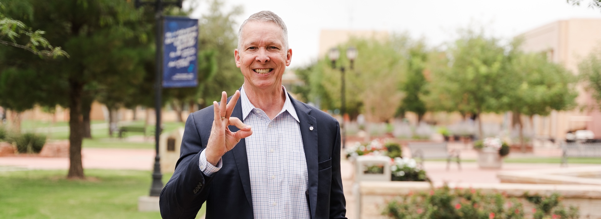 Photograph of Dr. McDowell holding up the "chap" handsign outside on LCU's campus