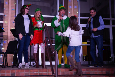 Christmas elf-themed characters handing a prize to a guest 